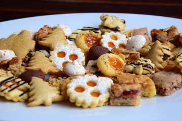 Bunt gemischte Weihnachtsplätzchen auf weißen Teller und dunklen Hintergrund