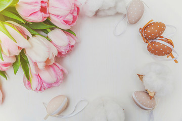 Spring greeting card. Easter eggs with moss cotton and pink fresh tulip flowers bouquet on rustic white wooden background. Easter concept. Flat lay top view copy space. Spring flowers tulips