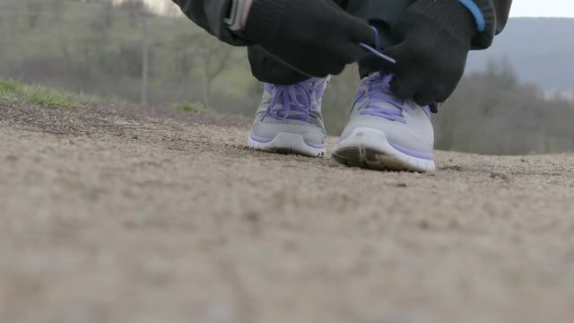 Male athlete runner in winter sportswear, gloves and fitness band tying laces for jogging on path in park and running out. Man ties shoelaces preparing for sprint. Sportsman getting ready for training