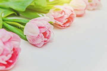 Fototapeta premium Spring greeting card. Bouquet of fresh light pastel pink tulips flowers on white wooden background. Happy holiday easter mother day anniversary valentine birthday concept. Flat lay top view copy space