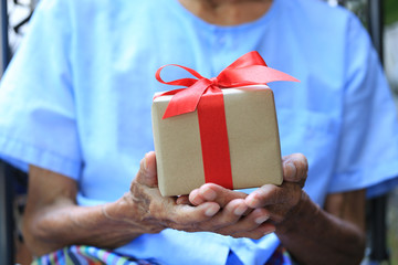 Senior man hands holding gift box with red ribbon for Christmas and New Year's Day or Greeting season