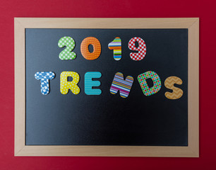 Black chalkboard with wooden frame, text 2019 trends in colorful numbers, red wall background