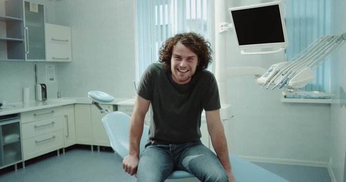 In a dental clinic room a man patient waiting for his dentis have a sit on dentis chair happy smiling large in front of the camera. 4k