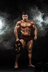 Fototapeta na wymiar Brutal strong muscular bodybuilder athletic man pumping up muscles with barbell on black background. Workout bodybuilding concept. Copy space for sport nutrition ads.