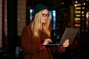 Hipster blond business woman owner with laptop any time of day has access to internet. Female student traveler sharing news mobile coverage helps to be always in touch over pub blurred interior
