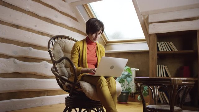 Attractive woman typing on laptop sitting in chair