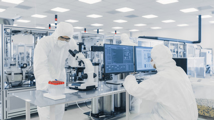 Team of Research Scientists in Sterile Suits Working with Computers, Looking Under Microscope and Modern Industrial Machinery in the Laboratory. Product Manufacturing Process: Semiconductors. - obrazy, fototapety, plakaty