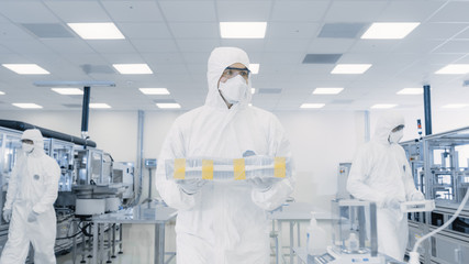 Scientist in Protective Suit Carries Case with Finished Product Through Laboratory. Facility with...