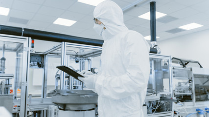 Quality Control Check: Scientist Using Digital Tablet Computer and wearing Protective Suit walks...