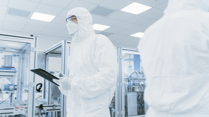 Quality Control Check: Scientist Using Digital Tablet Computer and wearing Protective Suit walks...