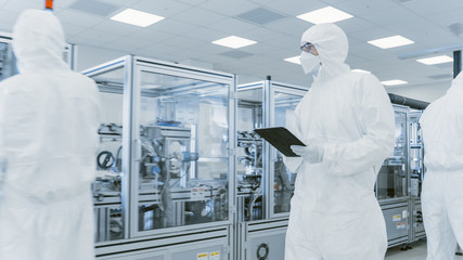 Quality Control Check: Scientist Using Digital Tablet Computer and wearing Protective Suit walks...