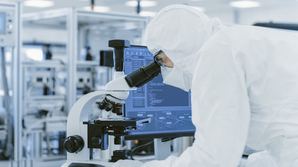 In Laboratory Scientist in Protective Clothes Doing Research Uses Microscope and Personal Computer....
