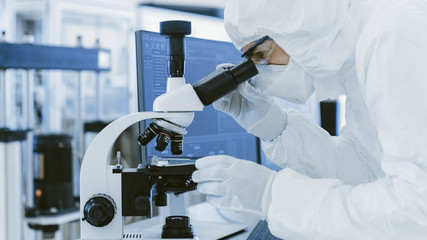 In Laboratory Scientist in Protective Clothes Doing Research Uses Microscope and Personal Computer....