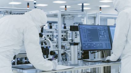 In Laboratory Scientists in Protective Clothes Doing Research, Using Microscope and Entering Data into Personal Computer. Modern Manufactory Producing Semiconductors and Pharmaceutical Items.