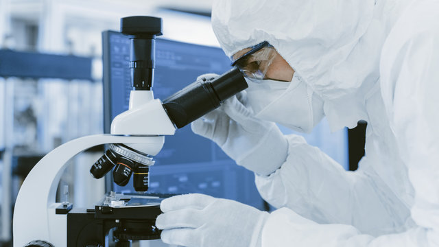 Close-up Shoy of a Scientist in Protective Clothes Doing Research Uses Microscope in Labolatory. Modern Manufactory Producing Semiconductors and Pharmaceutical Items.