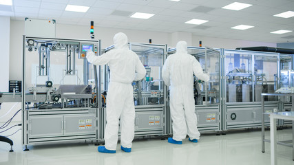 In the Manufacturing Facility Team of Scientist Wearing Sterile Protective Coverall Set's up / Programs Modern Industrial 3D Printer, High Precision Manufacture of Semiconductors under Process.