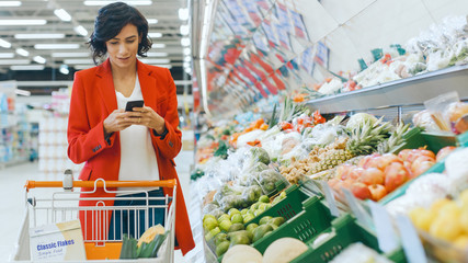 At the Supermarket: Young Woman Walks Through Fresh Produce Section, Chooses Vegetables and Pushing...