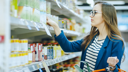 At the Supermarket: Beautiful Young Woman Browses through the Canned Goods Section of the Store....