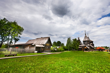 Fototapeta na wymiar Ancient wooden peasant house and a wooden church on the green grass