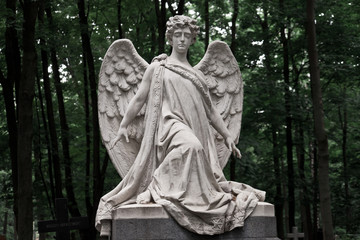 Fototapeta na wymiar The Sorrowful Angel. Marble mourning angel on a background of green foliage