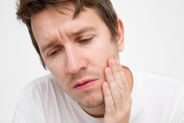 Adult young man's hand touching cheek. Feeling and suffering from terrible strong teeth pain. Closeup. Front view.
