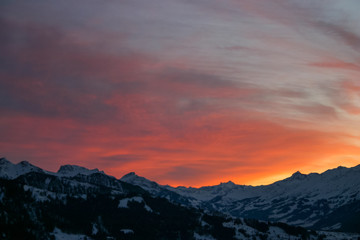shades of orange and pink clouds explode over the snow-capped Alps in this epic mountain sunset
