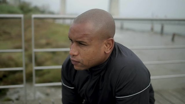 Confident sportsman stratching legs on wooden pier. Thoughtful bald man during outdoor workout. Healthy lifestyle concept