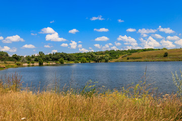 Fototapeta premium Summer landscape with beautiful lake, green meadows, hills, trees and blue sky