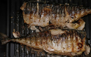 Mackerel is roasted on an electric grill. Grilled fish with lemon and salad