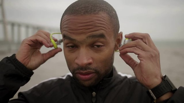 Handsome young man wearing wireless earphones. African american man with bristle preparing to training. Technology concet