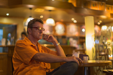 Man in a Cafe in a ill-humored mood contemplative staring and wearing a orange shirt stare into space