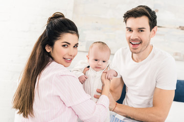 parents and little baby resting on bed together at home