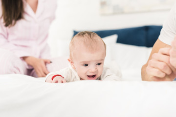 partial view of parents and little baby lying on bed together at home