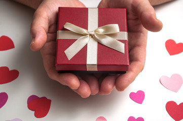 closeup of red gift in shaped heart in hand of woman on white table background - valentine's day concept