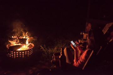 a woman on a smartphone outside while enjoying a warm fire