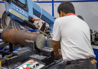 Industrial technician operate band saw machine cutting metal work piece with coolant. Industrial...