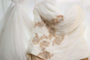 Details of the bride's white and gold wedding dress hanging on a four poster bed