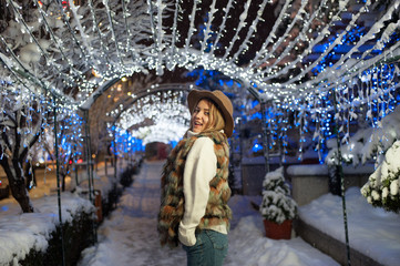 Pretty girl wearing blue jeans and a white top with snowflakes Christmas lights outdoor at night time.