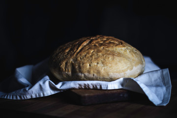 Bread on a wooden plane - Freshly baked homemade bread left to cool on a white kitchen towel - Bio  and healthy food concept - Dark background and vintage color style.