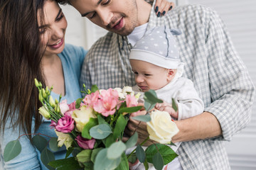 portrait of happy parents with little son and bouquet of flowers at home