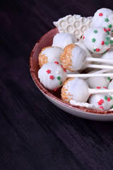 Cake pops covered in white chocolate and multicoloured sprinkles on a plate against the dark background