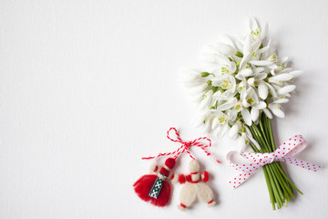  A bouquet of snowdrops on a white canvas and a red-white martenitsa, a symbol of the holiday on March 1, Martisor, Baba Marta.