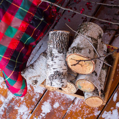 A stack of birch wood near the sofa with a red checkered rug on the open winter snowy terrace.  Top view