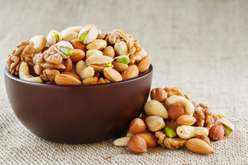 Mix of different nuts in a wooden cup against the background of fabric from burlap. Nuts as structure and background, macro. Top view.