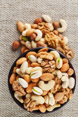Mix of different nuts in a wooden cup against the background of fabric from burlap. Nuts as structure and background, macro. Top view.