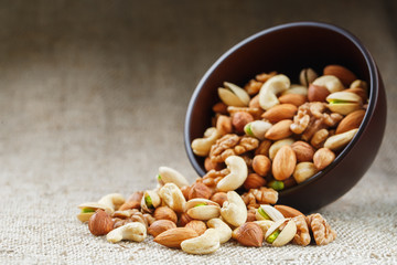 Mix of different nuts in a wooden cup against the background of fabric from burlap. Nuts as structure and background, macro. Top view.