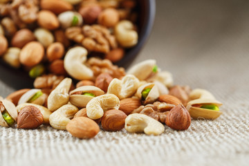 Mix of different nuts in a wooden cup against the background of fabric from burlap. Nuts as structure and background, macro. Top view.