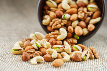 Mix of different nuts in a wooden cup against the background of fabric from burlap. Nuts as structure and background, macro. Top view.