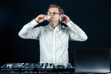 DJ trinkt ein Glas Sekt am Mischpult während er seine Tracks hört