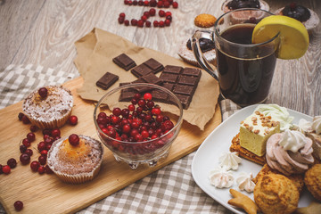 Fototapeta na wymiar On a light wooden tabletop on a linen napkin napkin, there is a cutting board with two muffins, a broken chocolate bar and bright red berries in a small tree, next to a bowl with cookies. On a light